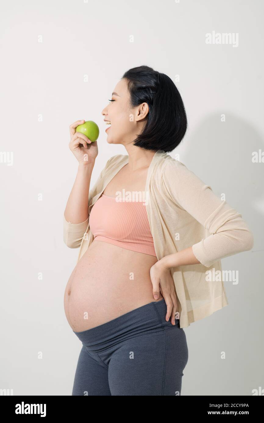 Nur einen Apfel am Tag. Schöne junge schwangere Frau mit Lächeln und hält grünen Apfel, während auf weißem Hintergrund stehen Stockfoto