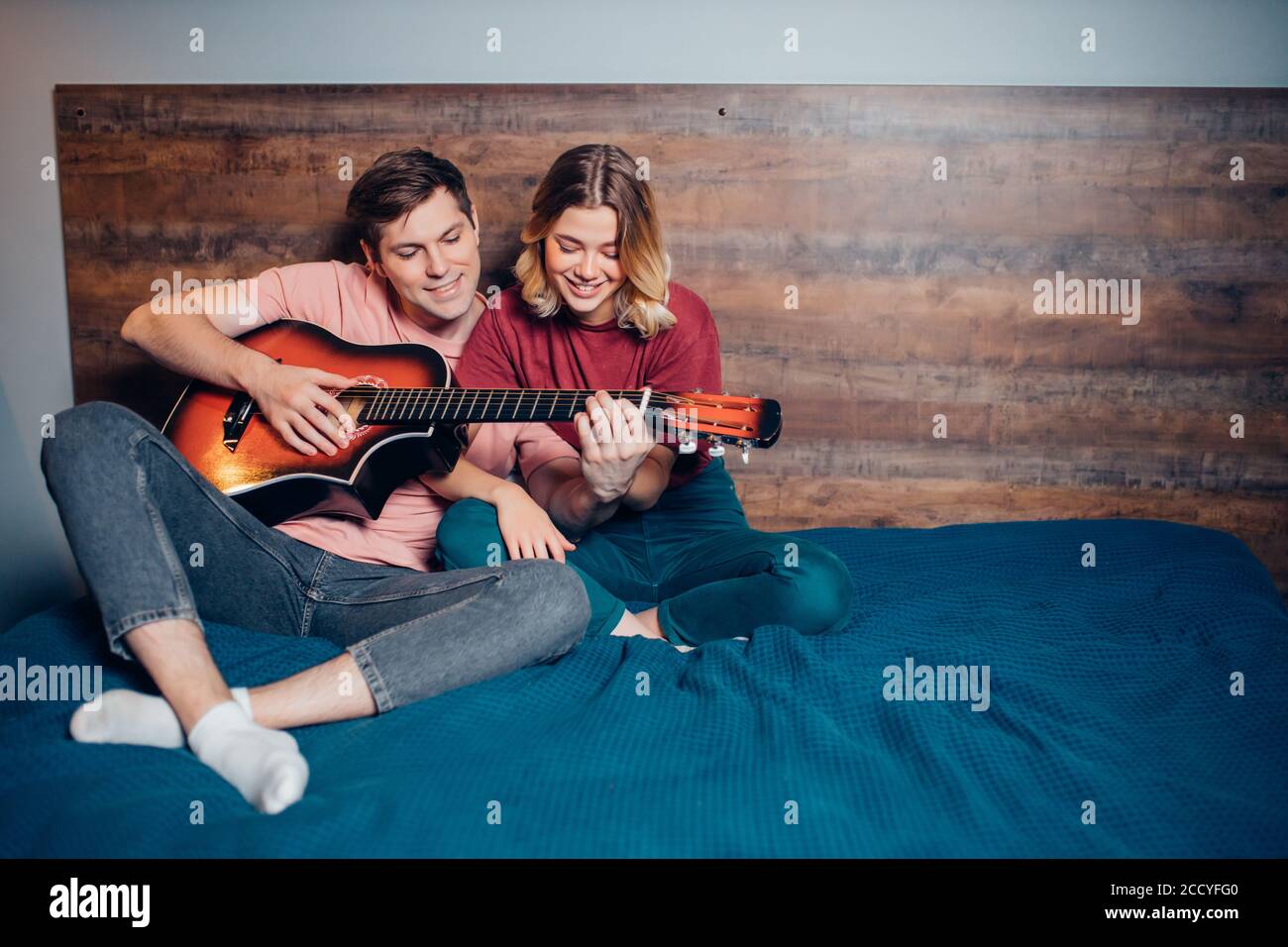 Zwei romantische Menschen in der Liebe sitzen zusammen auf dem Bett, spielen die Gitarre. kaukasische Menschen sitzen zusammen zu Hause Stockfoto