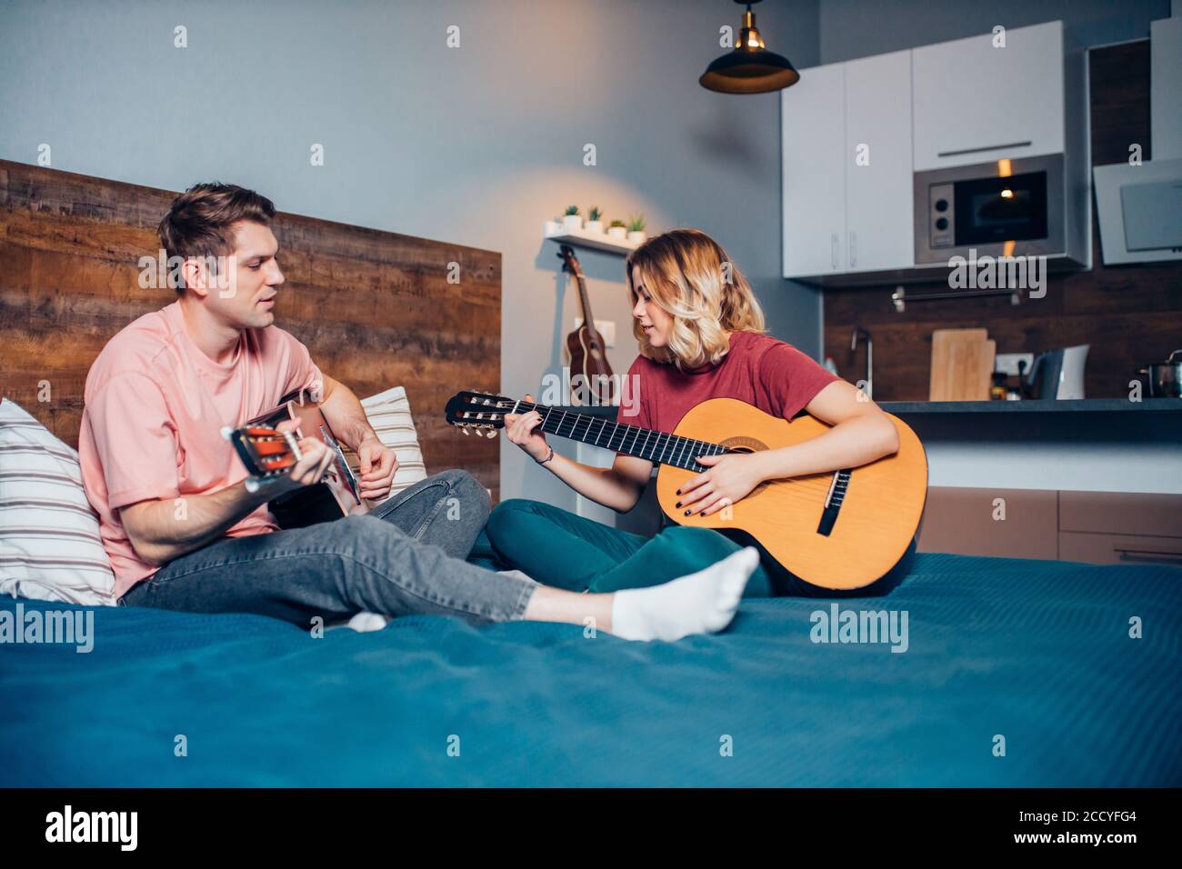 Zwei romantische Menschen in der Liebe sitzen zusammen auf dem Bett, spielen die Gitarre. kaukasische Menschen sitzen zusammen zu Hause Stockfoto