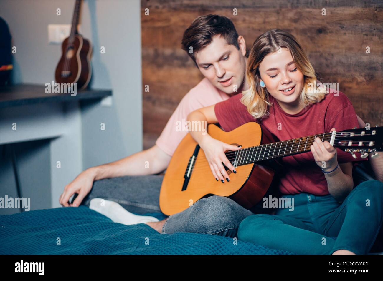 Zwei romantische Menschen in der Liebe sitzen zusammen auf dem Bett, spielen die Gitarre. kaukasische Menschen sitzen zusammen zu Hause Stockfoto