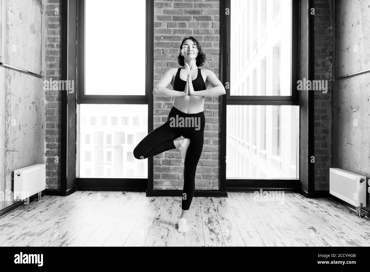 Fröhliche motivierte Frau steht auf einem Bein und praktiziert Yoga. Schwarz-weiß Foto.Motivation und Gesundheitsversorgung Stockfoto