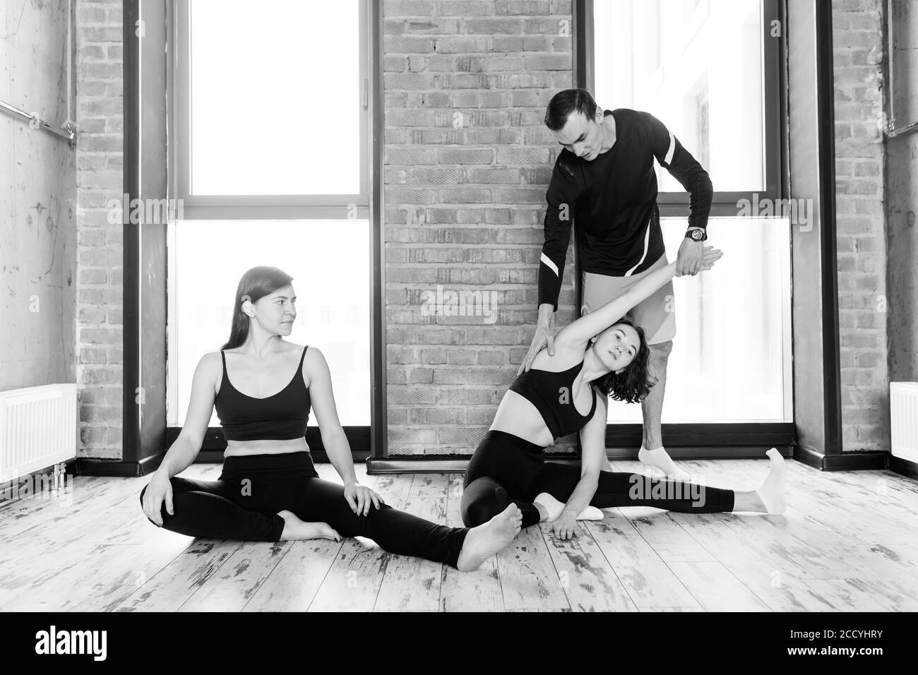 Zwei fittige Mädchen trainieren mit Personal Trainer in der Fitness-Klasse. Schwarz-Weiß-Foto Stockfoto