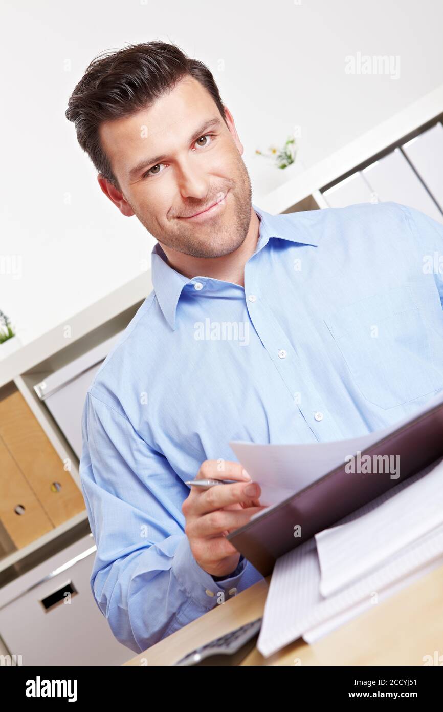 Lächelnder Bankberater mit Dokumenten im Büro am Schreibtisch Stockfoto