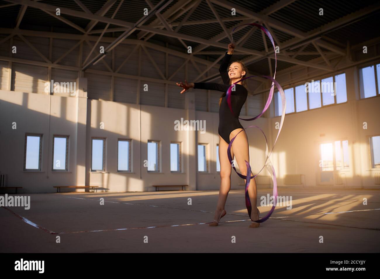 Spielerisch fröhlich weibliche Turnerin Durchführung rhythmische Gymnastik Element auf Wettbewerb, Tanz mit bunten Band, Stretching Hand voraus, Blick auf ein Stockfoto