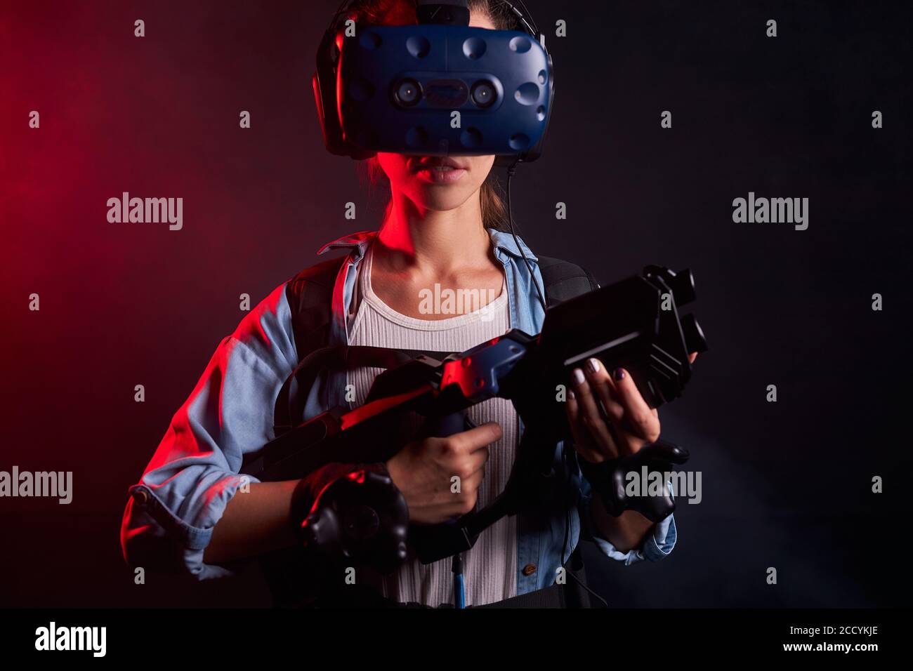 Junge kaukasische Frau hält Shooter VR, tragen Augenmaske, stehen isoliert über UV-Hintergrund Stockfoto
