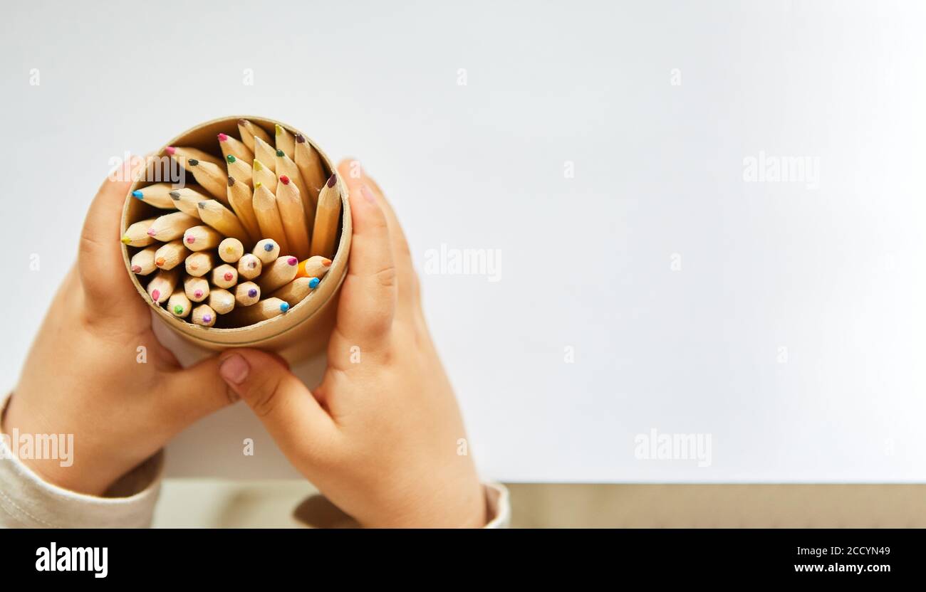 Hände eines Kleinkindes halten einen Becher mit viel Buntstifte Stockfoto