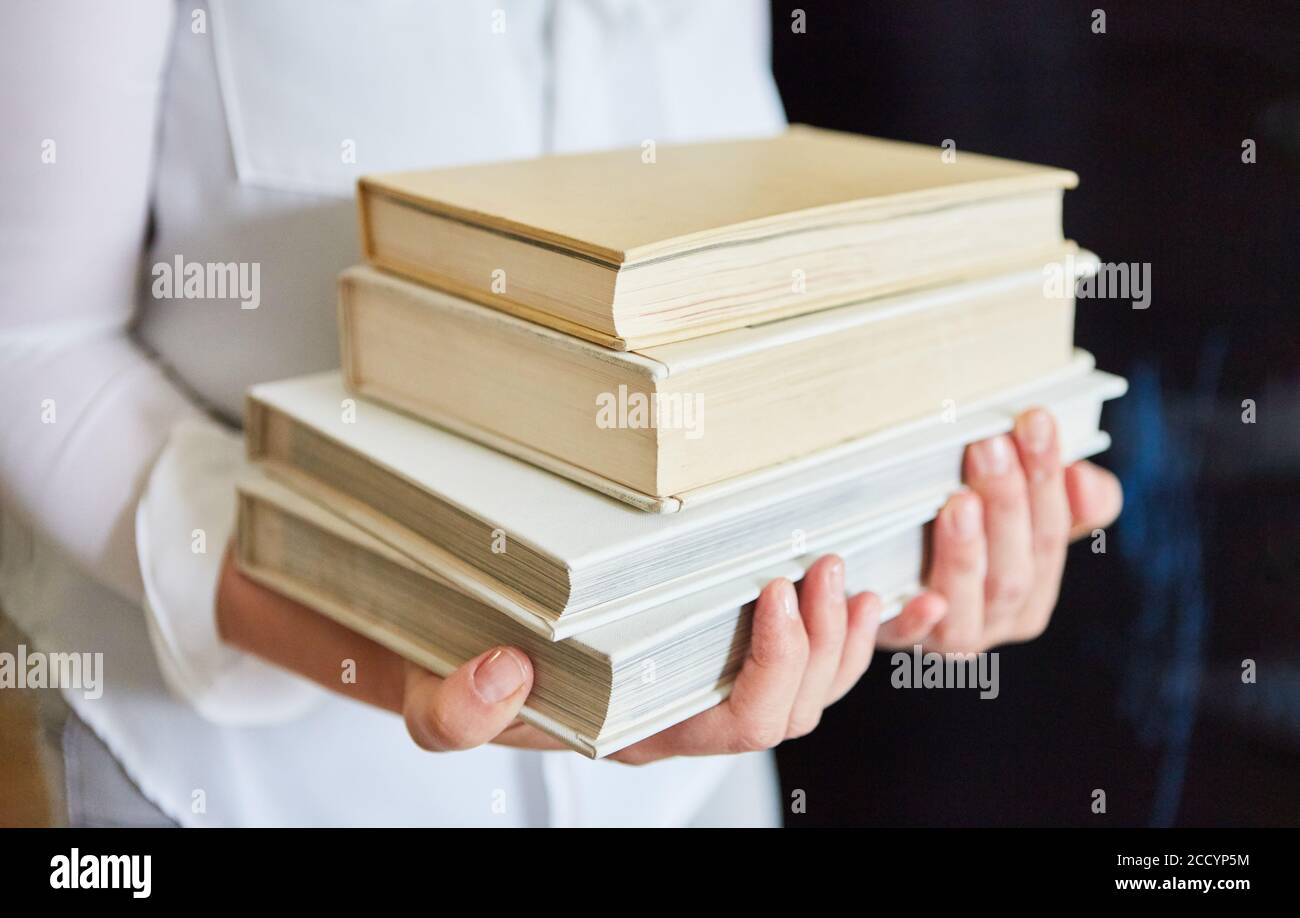 Frau trägt einen Stapel alter Bücher in einem gebrauchten Buchladen oder Bibliothek Stockfoto