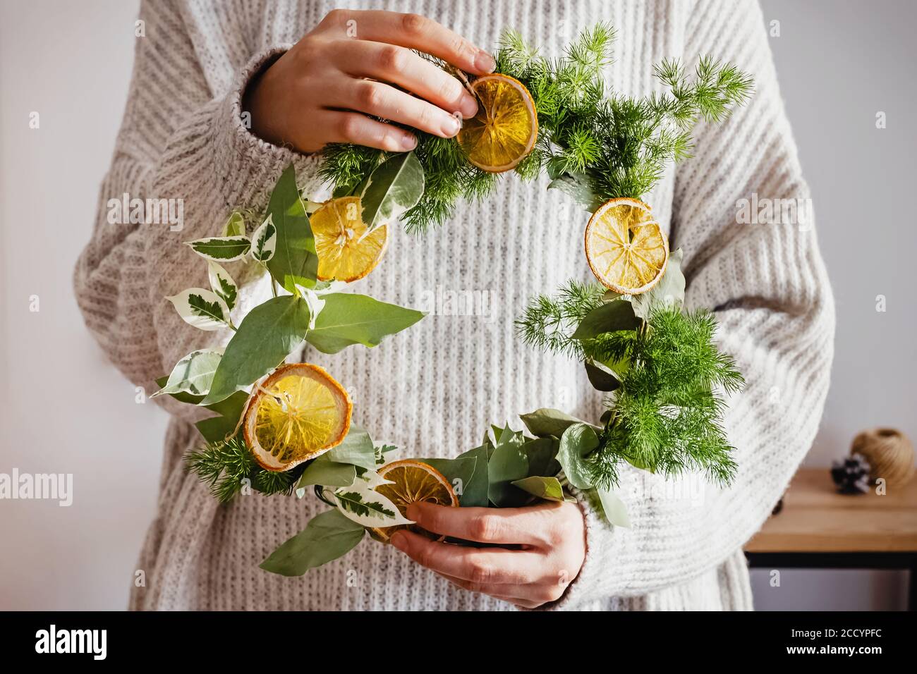 Frau in gestricktem Pullover mit einem handgefertigten Weihnachtskranz. Stockfoto