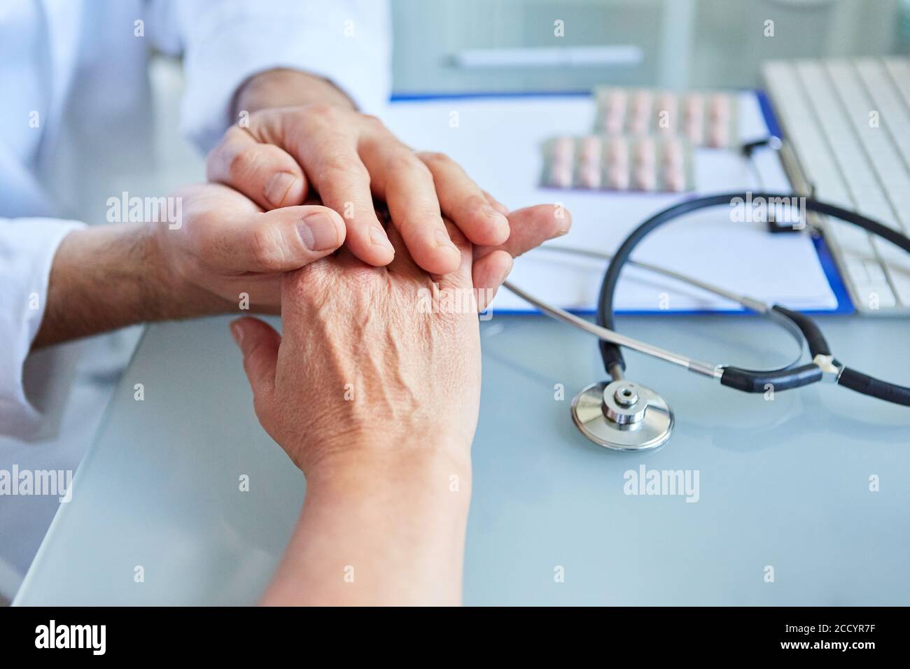 Hausarzt hält die Hand eines Patienten in beiden Hände in der Sprechstunde Stockfoto