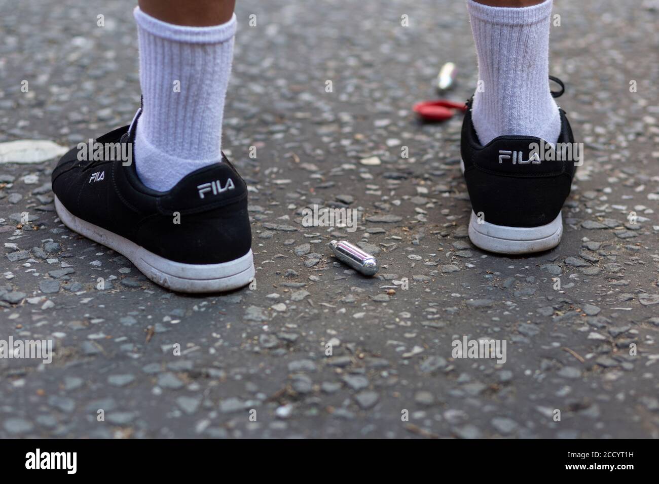 Blick auf die Füße einer Person, die während des Notting Hill Carnival, London, 2019 neben ausrangierten Nitrosoxid-Kanistern auf einer Straße steht Stockfoto