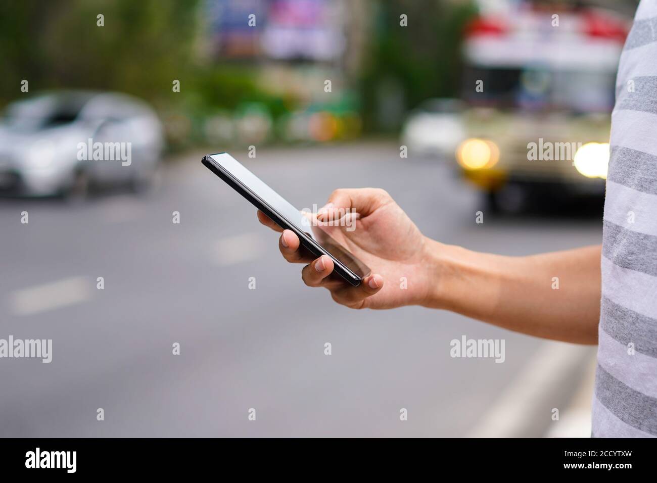 Hand des Mannes mit einem Handy auf der Straße. Nutzung der Transport App. Stockfoto
