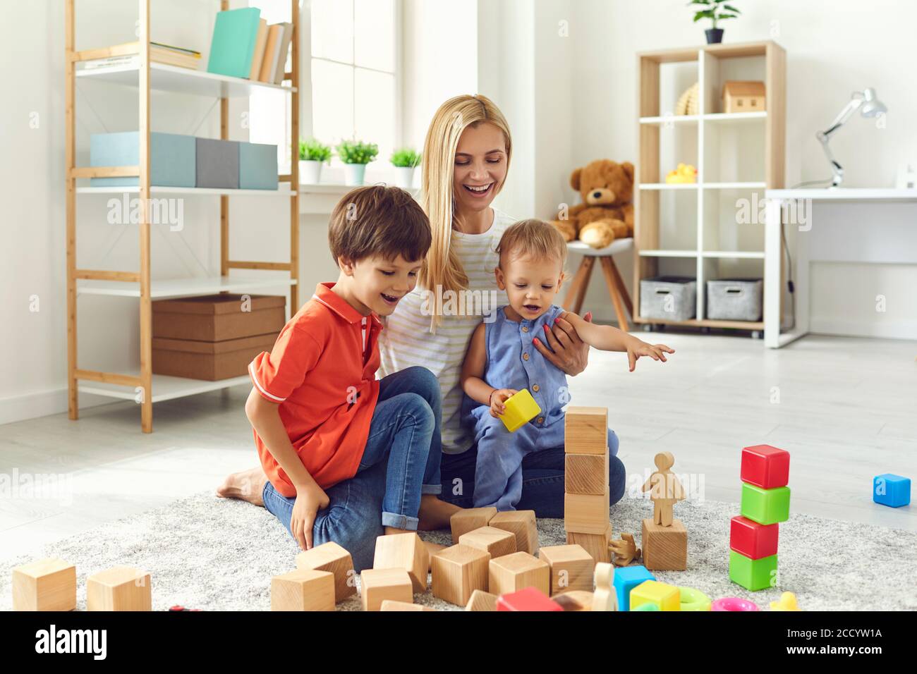 Mama und Kinder lächeln mit Spielzeug, während sie auf dem Boden im Wohnzimmer sitzen. Frohe Familie Stockfoto