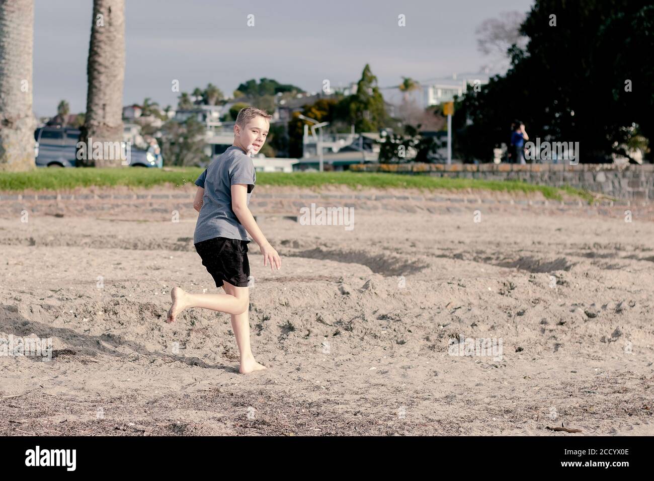 Ein kleiner Junge, der am Strand rennt und nach hinten über seine Schulter schaut. Stockfoto