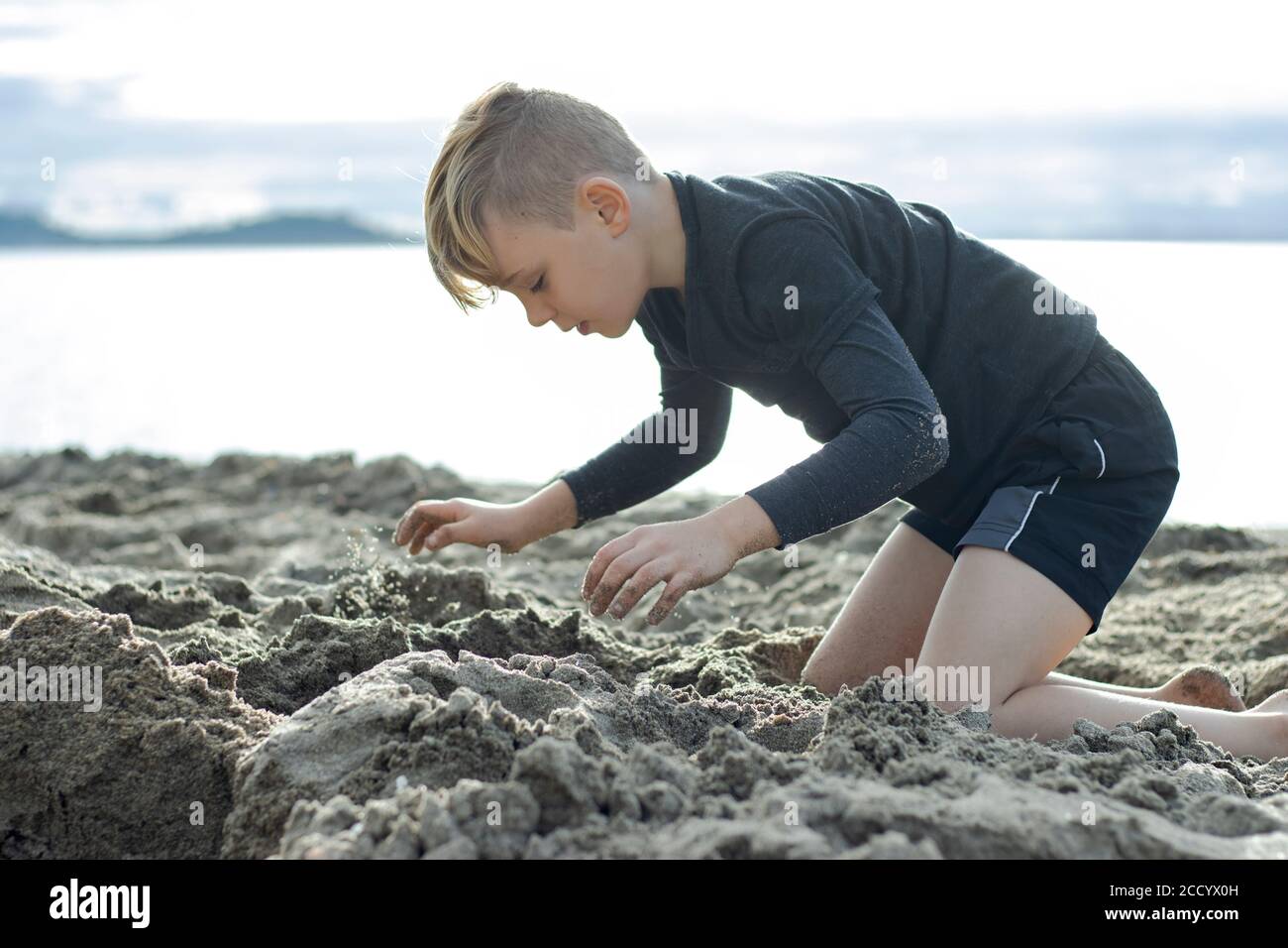 Eine Nahaufnahme eines wunderschönen Jungen, der im Sand am Strand spielt, seine Augen vor Freude verschlossen Stockfoto