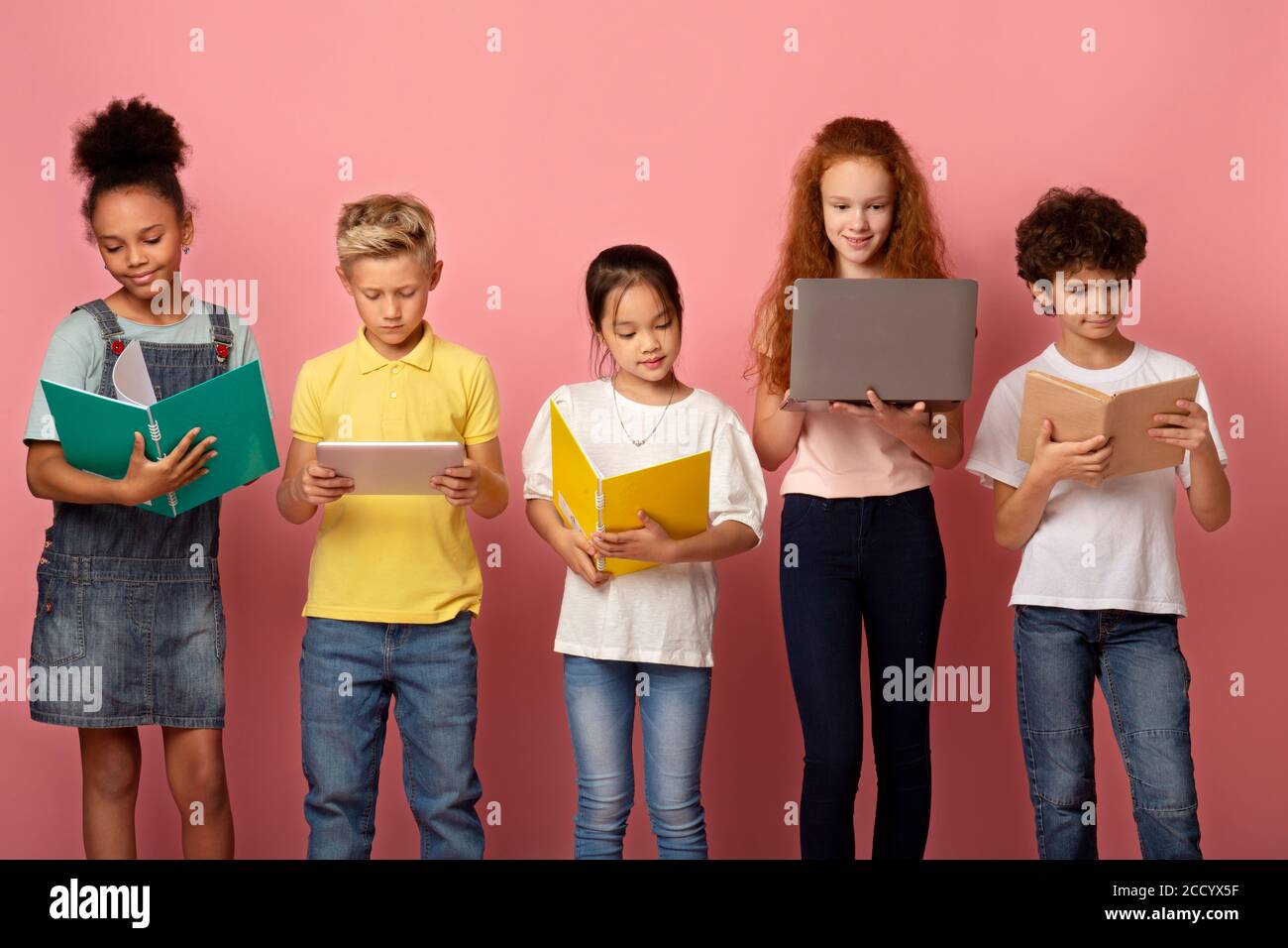 Fleißige junge Schüler mit Notizbüchern, Büchern und Gadgets konzentrierten sich auf das Studium auf rosa Hintergrund Stockfoto