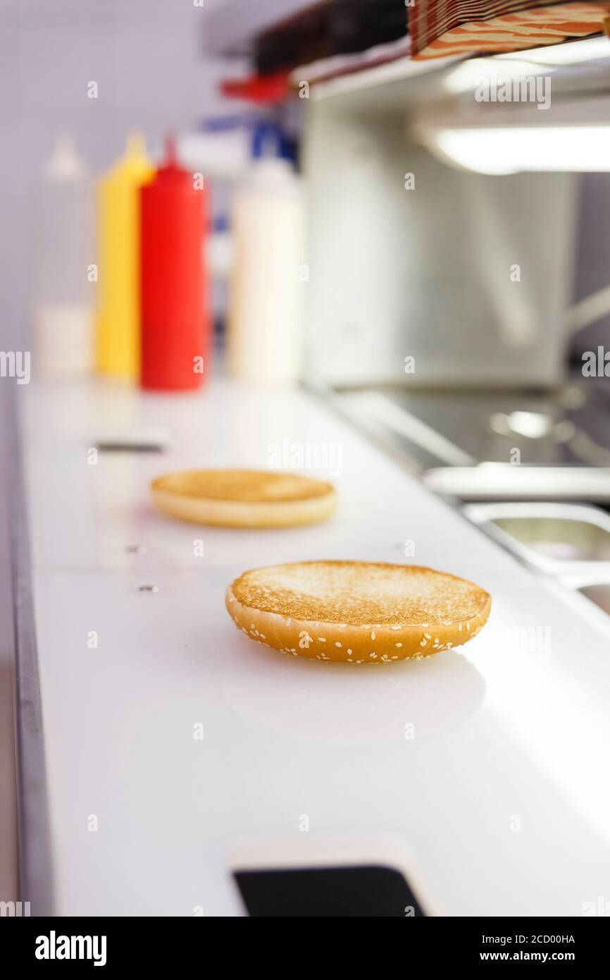 Das Hamburgerbrötchen befindet sich auf der Arbeitsfläche des Kochs. Daneben befinden sich Edelstahlbehälter mit Kochzutaten. Stockfoto