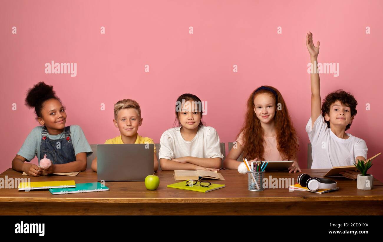 Smart kaukasischen Jungen und seine Freunde bereit, Unterricht am Tisch vor rosa Hintergrund zu beantworten, kopieren Raum Stockfoto