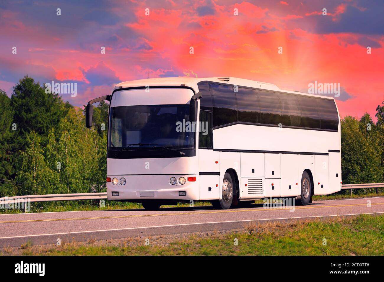 Weißer Reisebus fährt entlang der Autobahn bei Sonnenuntergang im Sommer. Stockfoto