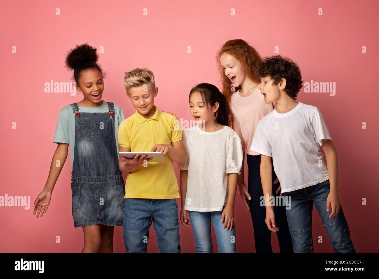 Aufgeregt Schüler und Schülerinnen Blick auf Tablet-Computer auf rosa Hintergrund Stockfoto