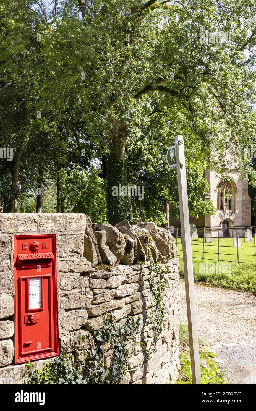 Ein ländlicher Briefkasten und Wegweiser neben der Kirche St. John the Evangelist im Cotswold Dorf Elkstone, Gloucestershire UK Stockfoto