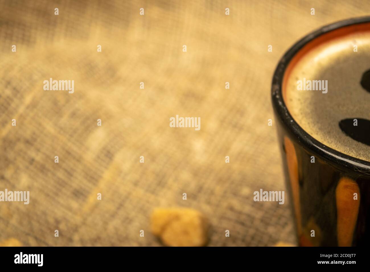Tasse Kaffee und Scheiben braunen Rohrzuckers auf einem Hintergrund von homespun Stoff mit einer rauen Textur. Nahaufnahme Stockfoto