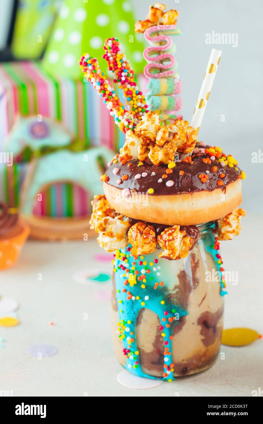 Kids Party Konzept: Schokofreak Shake Belag mit Donut und Karamell Popcorn auf dem Partytisch neben Rocker Pferd Spielzeug und Geschenk-Boxen; selektiv Stockfoto