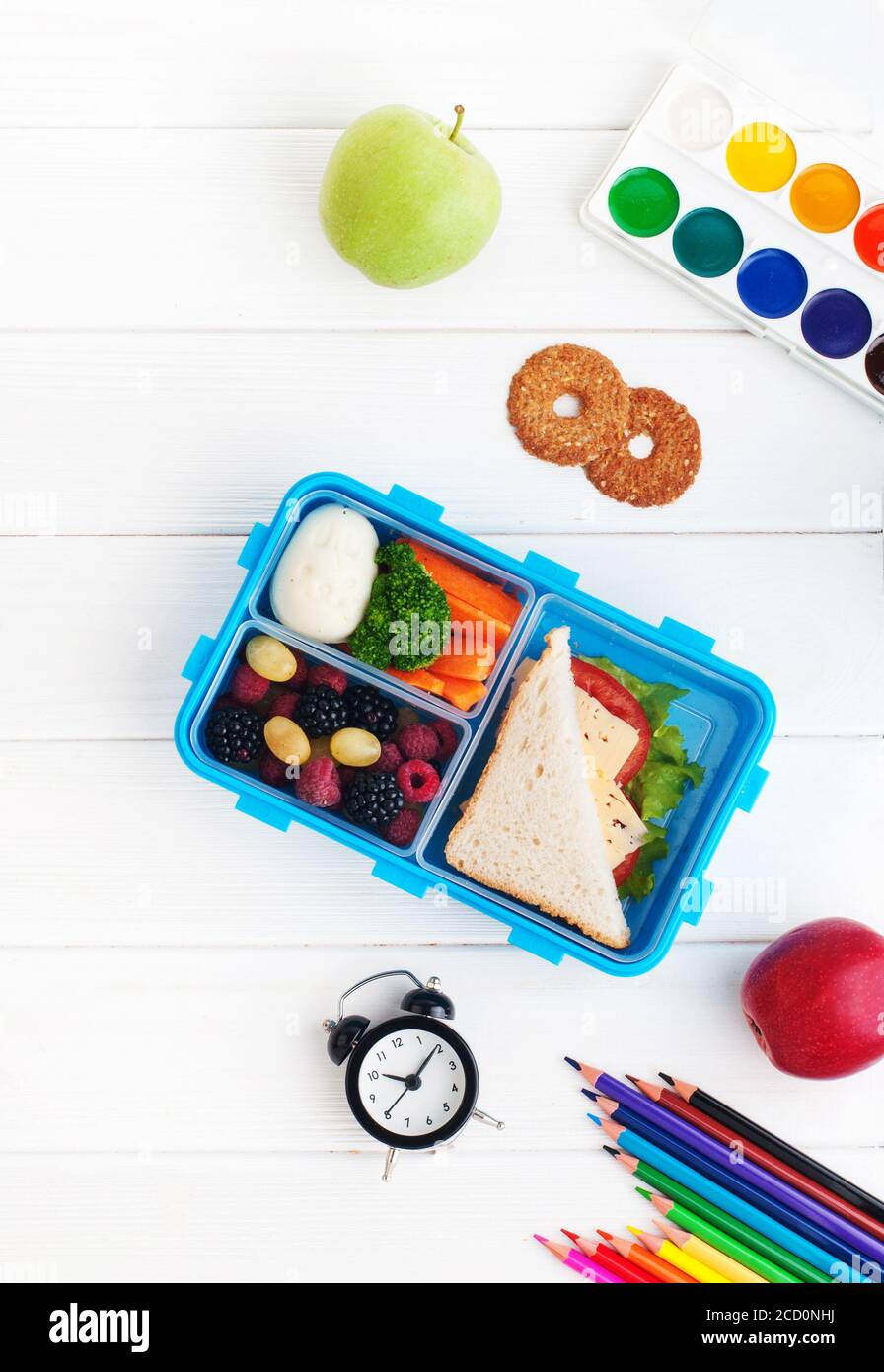 Offene Lunchbox mit Sandwich, Gemüse, Ei, frischen Beeren mit Uhr, Aquarell und Bleistiften auf weißem Holzhintergrund. Draufsicht, flach liegend. Stockfoto