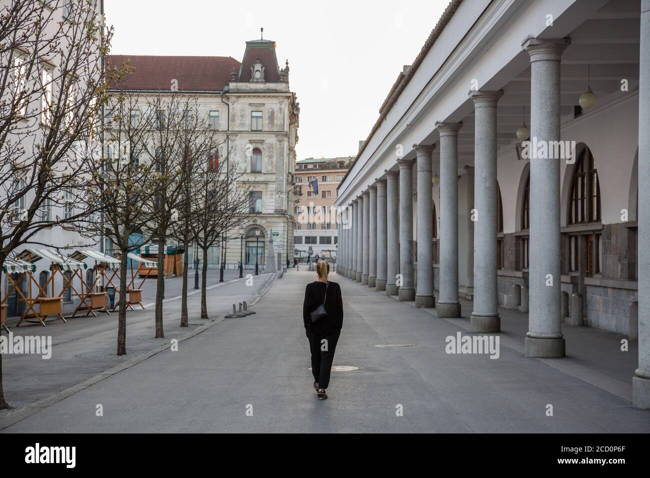 Rückansicht einer nicht erkennbaren Frau, die während einer Corona-Virus-Pandemie im leeren, mittelalterlichen Stadtzentrum von Ljubljana unterwegs ist. Fast keine Leute draußen auf Stockfoto