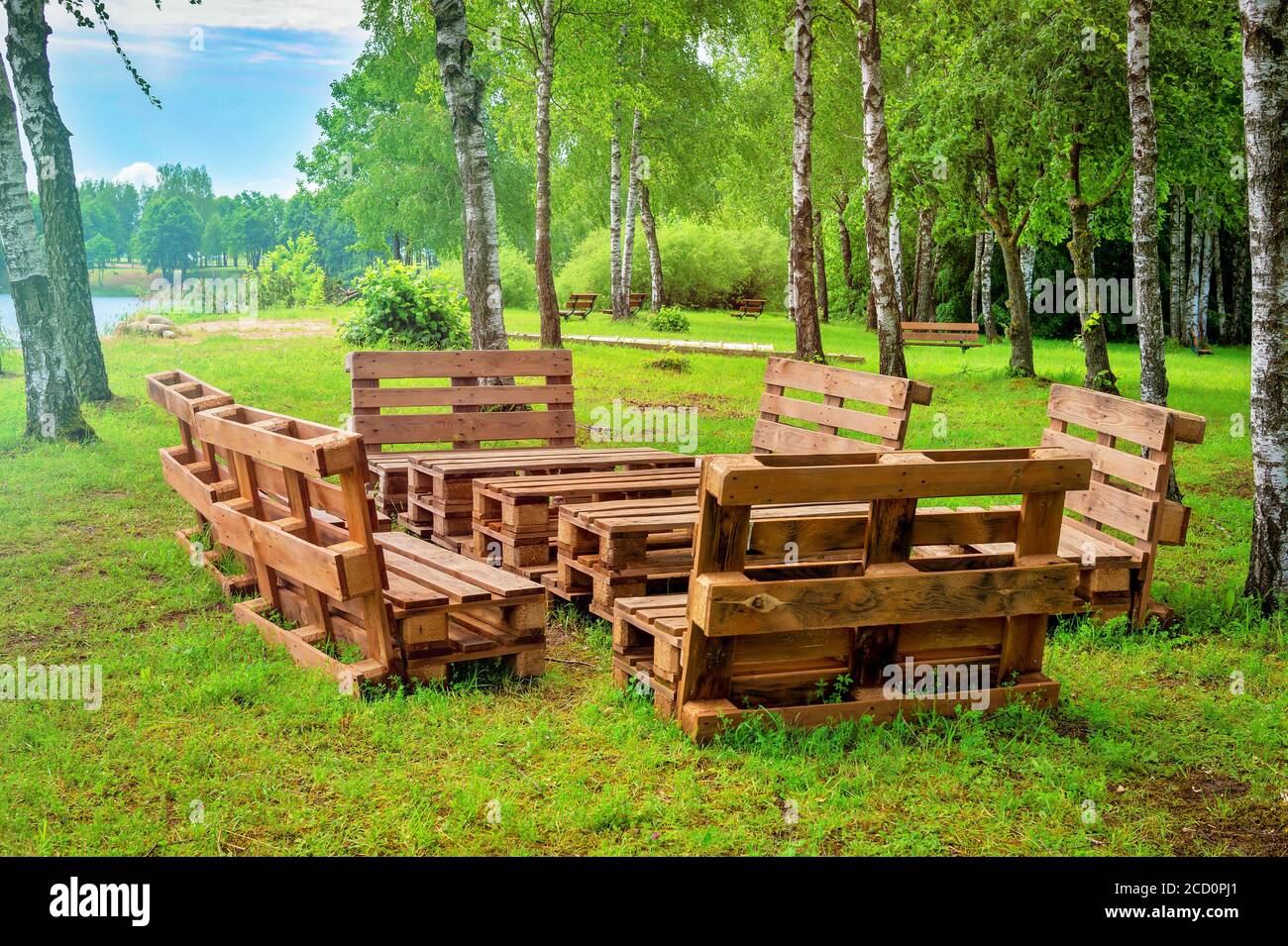 Gartenmöbel aus Holzpaletten, umgeben von Bäumen und Grün in der Sommersonne Stockfoto
