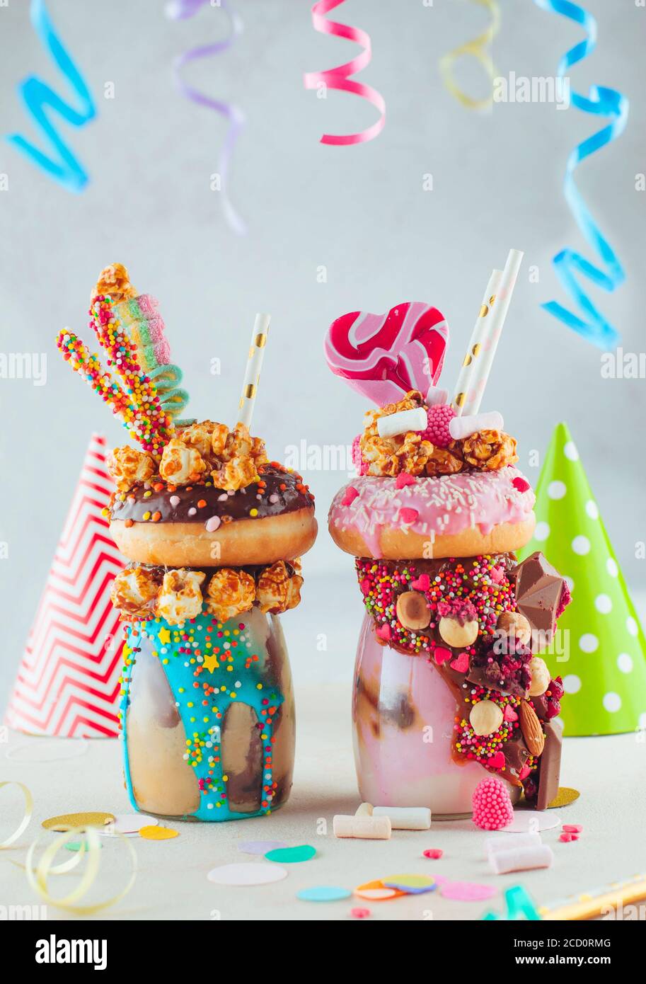 Zwei Freak-Shakes mit Donuts, Karamell-Popcorn und Süßigkeiten auf dem Kinderparty-Tisch; selektiver Fokus. Stockfoto