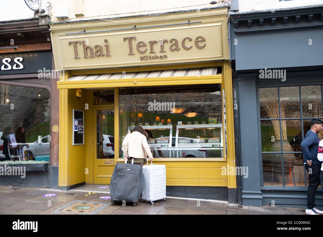 Windsor, Berkshire, Großbritannien - 25. August 2020. Eine obdachlose Dame rollt ihre weltlichen Besitztümer in zwei Koffern und schaut sehnsüchtig in einem Restaurantfenster auf das Buffetessen. Quelle: Maureen McLean/Alamy Live News Stockfoto