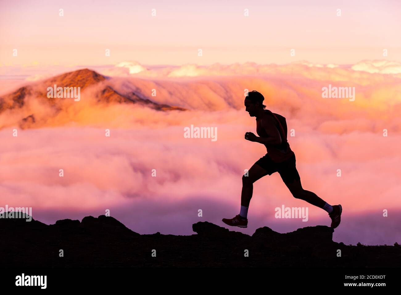 Trailrunner Athlet Mann Laufen in der Natur Landschaft. Silhouette des männlichen Menschen Training auf Bergen bei kaltem Wetter mit rosa Wolken bei Sonnenuntergang Stockfoto