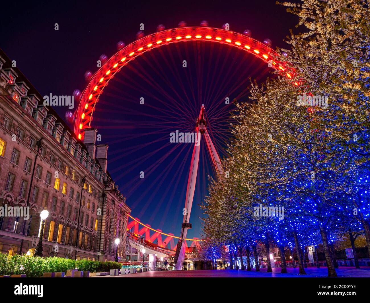 Das London Eye mit Bewegung verschwimmen in der Winterdämmerung mit roten Sponsoring Farbe Lichter in Bäumen atmosphärischen South Bank London, England Großbritannien Stockfoto