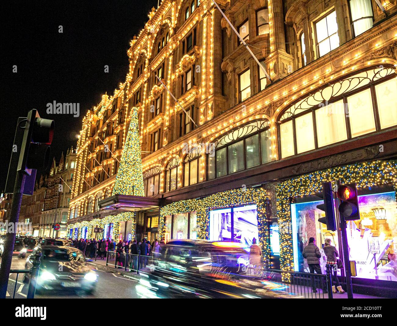 WEIHNACHTSEINKÄUFE LONDON HARRODS BAUMKÄUFER LONDON Harrods Kaufhaus in der Abenddämmerung mit Weihnachtslichtern, Einkaufsbummel und vorbeifahrenden Autos Knightsbridge London SW1 Stockfoto