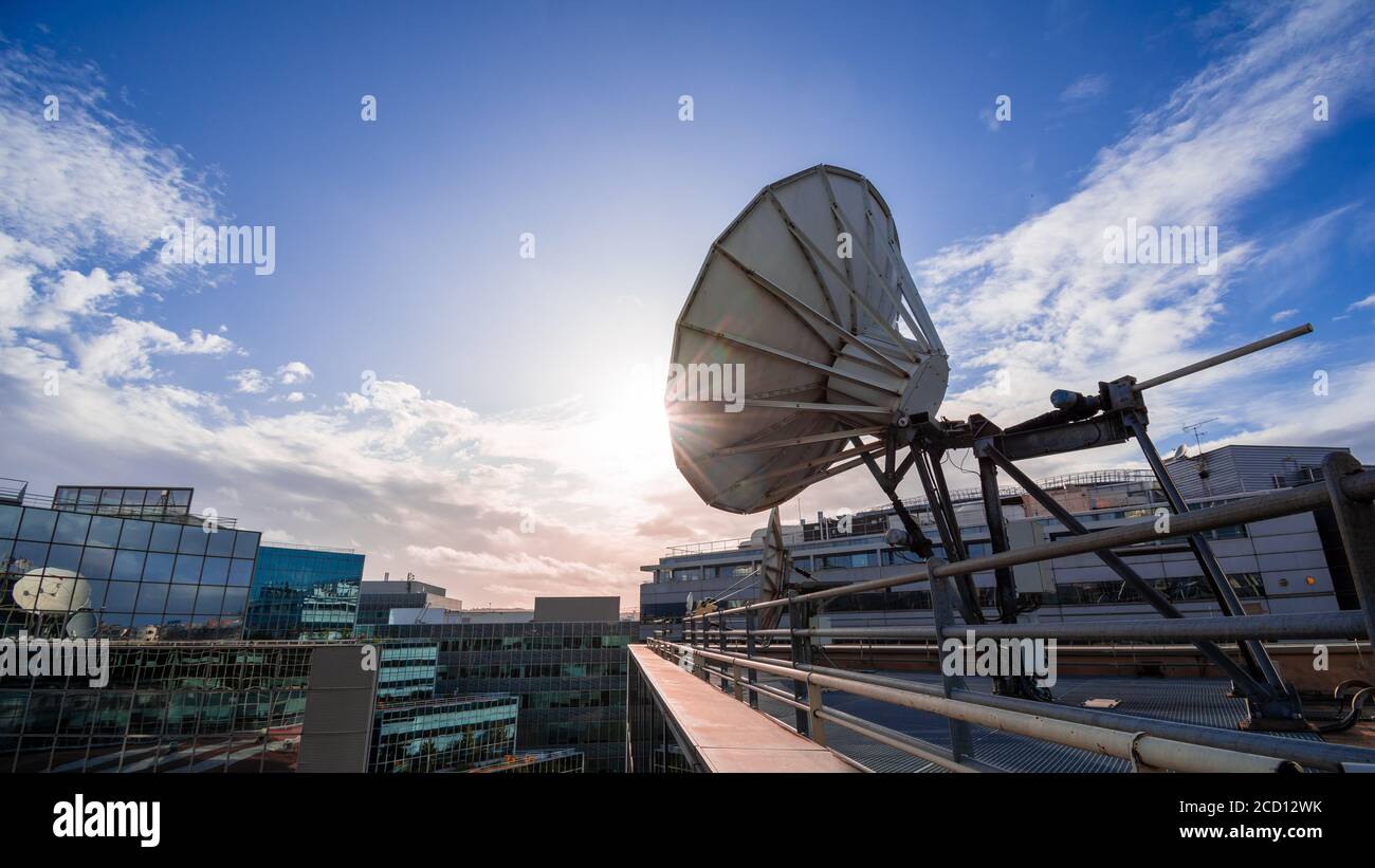 Satellitenschüssel in einem modernen Bürogebäude, blauer Himmel und untergehende Sonne. Konzept der Fernkommunikation Stockfoto