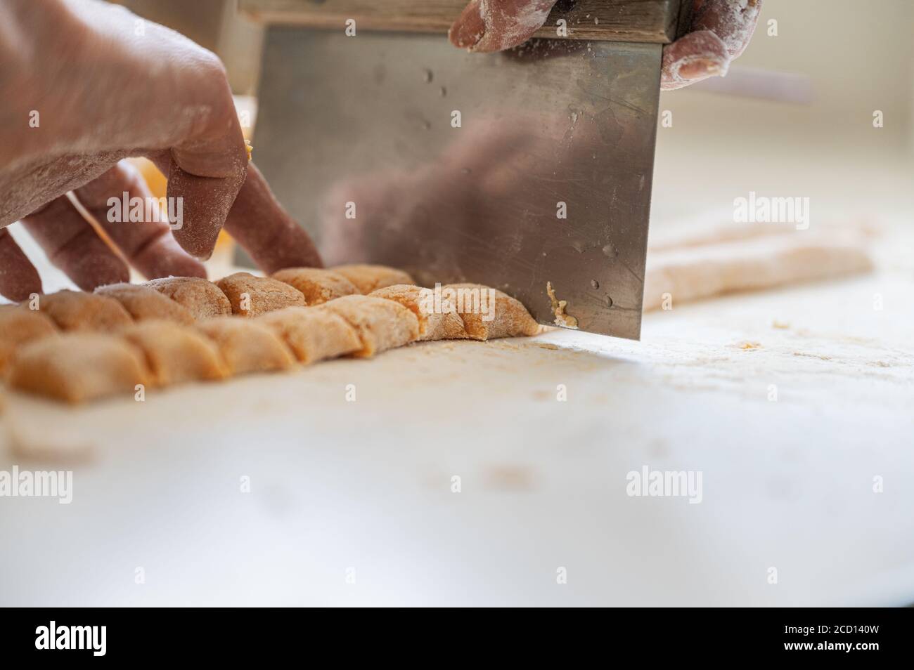 Nahaufnahme der weiblichen Hände, die frischen hausgemachten Nudelteig schneiden, um vegane Gnocchi zu machen. Stockfoto