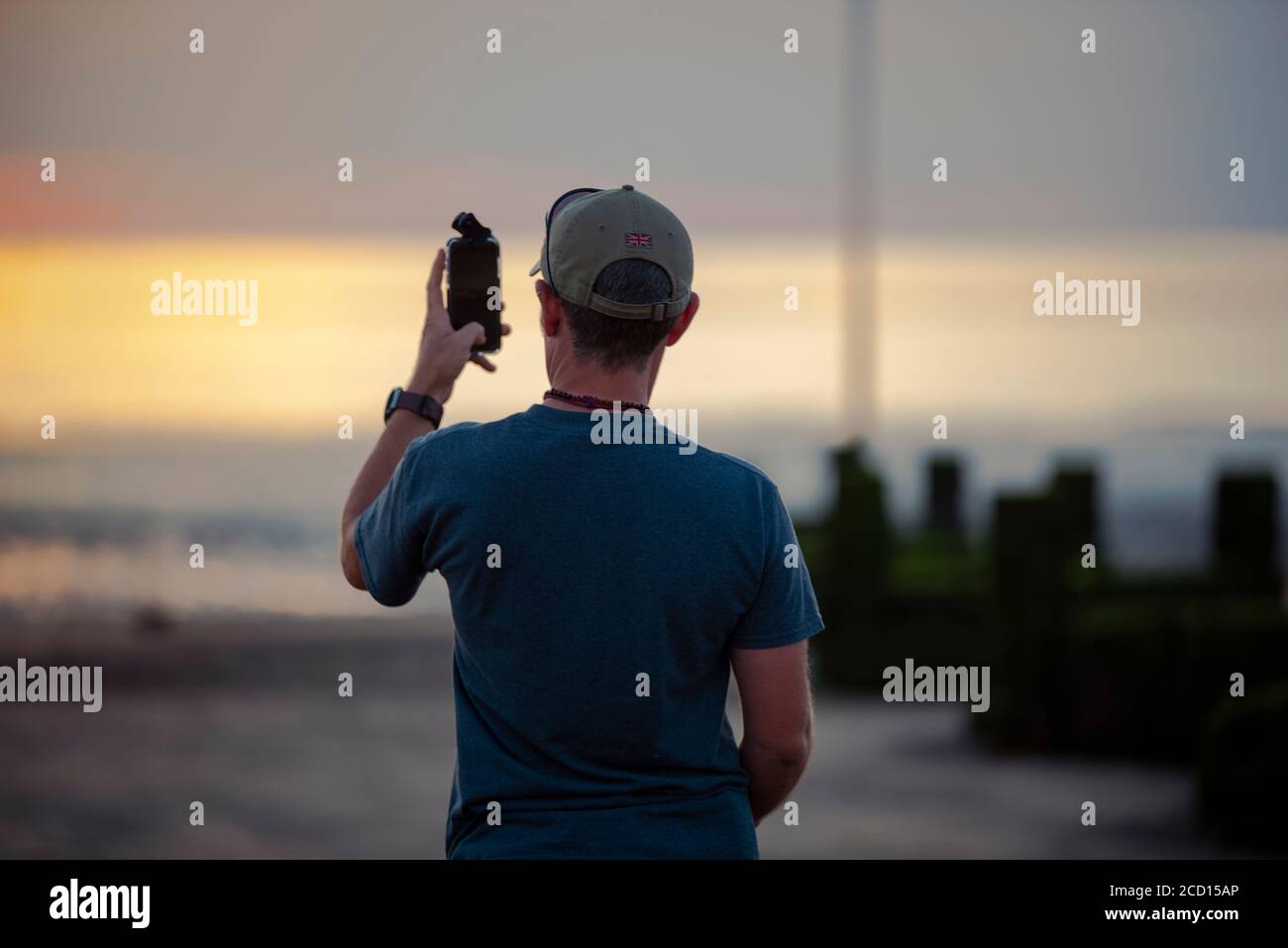Mann fotografiert den Sonnenuntergang mit seinem Handy am Hunstanton Beach Stockfoto