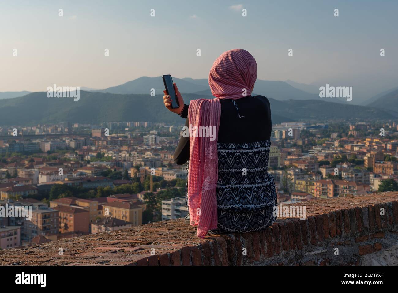 Ägyptisches Mädchen mit Smartphon auf der Dachterrasse mit Luftaufnahme der alten italienischen Stadt Brescia. Stockfoto