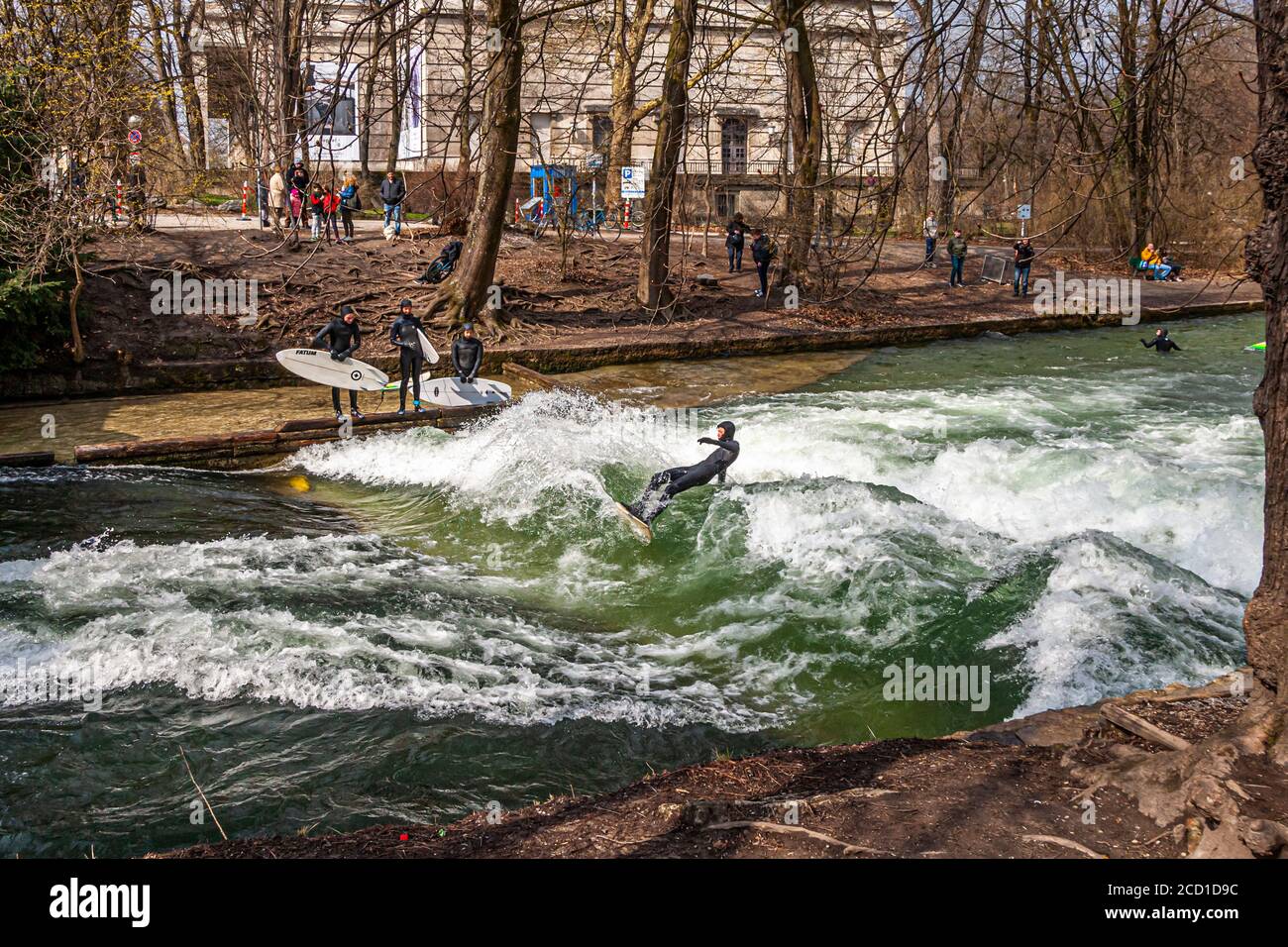 River-Surfing auf dem Eisbach in Mnchen, Deutschland. Die stehende Welle  kann so lange gesurft werden, wie das Gleichgewicht hlt, und in  geschftigen Zeiten bildet sich eine Schlange von Surfern am Ufer  Stockfotografie -