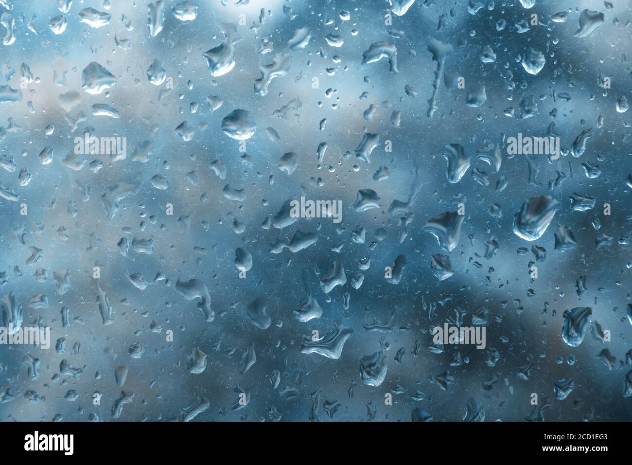 Regentropfen auf Glasscheibe mit verschwommenem dunkelblauem Hintergrund im Herbst. Wunderschöne Aussicht vom Fenster an regnerischen Tagen. Wassertropfen auf Glas mit verschwommenen Kanten. Stockfoto
