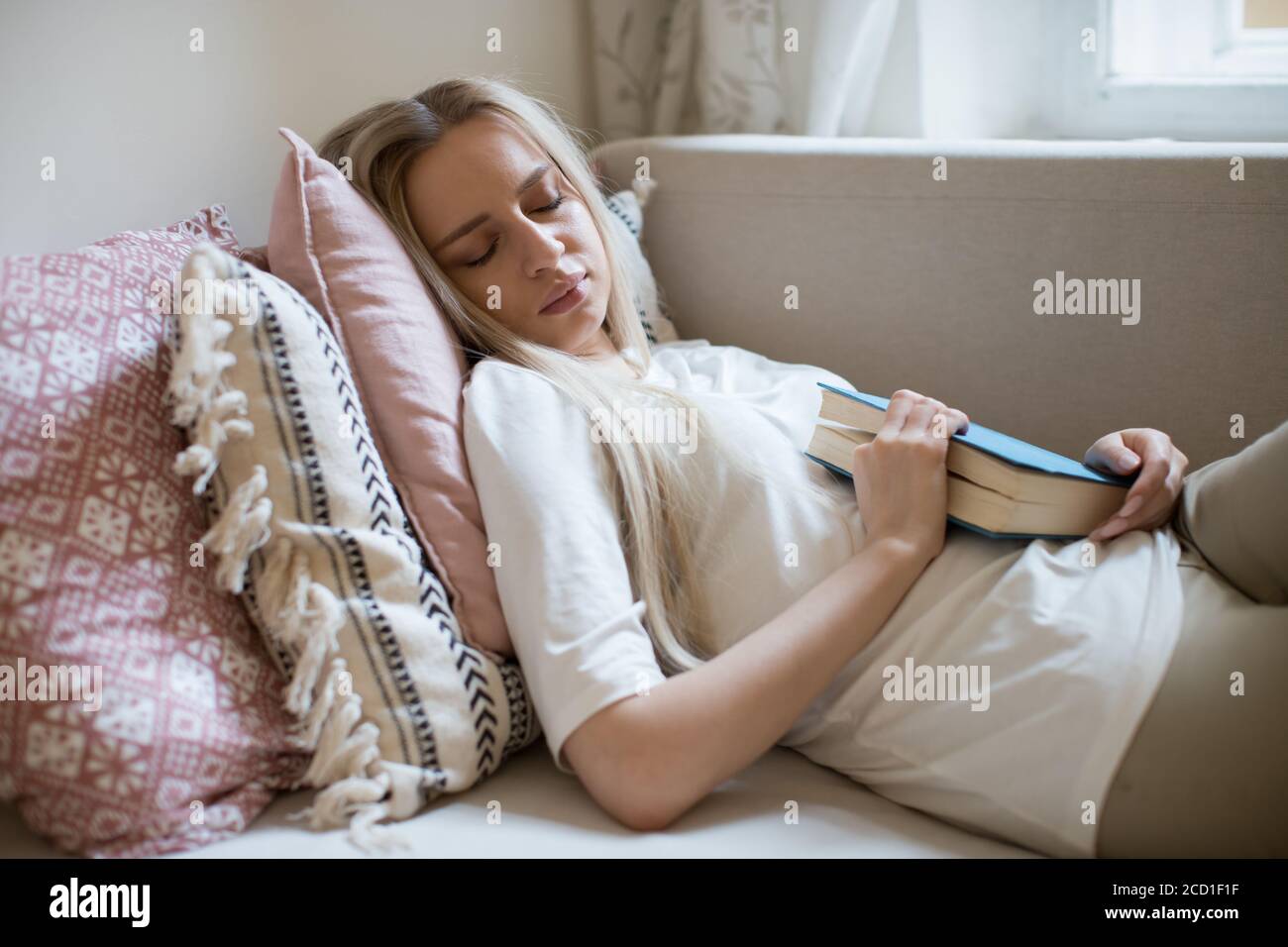 Müde Frau fühlte einen Schlaf mit Buch in den Händen liegend auf Sofa drinnen. Stockfoto