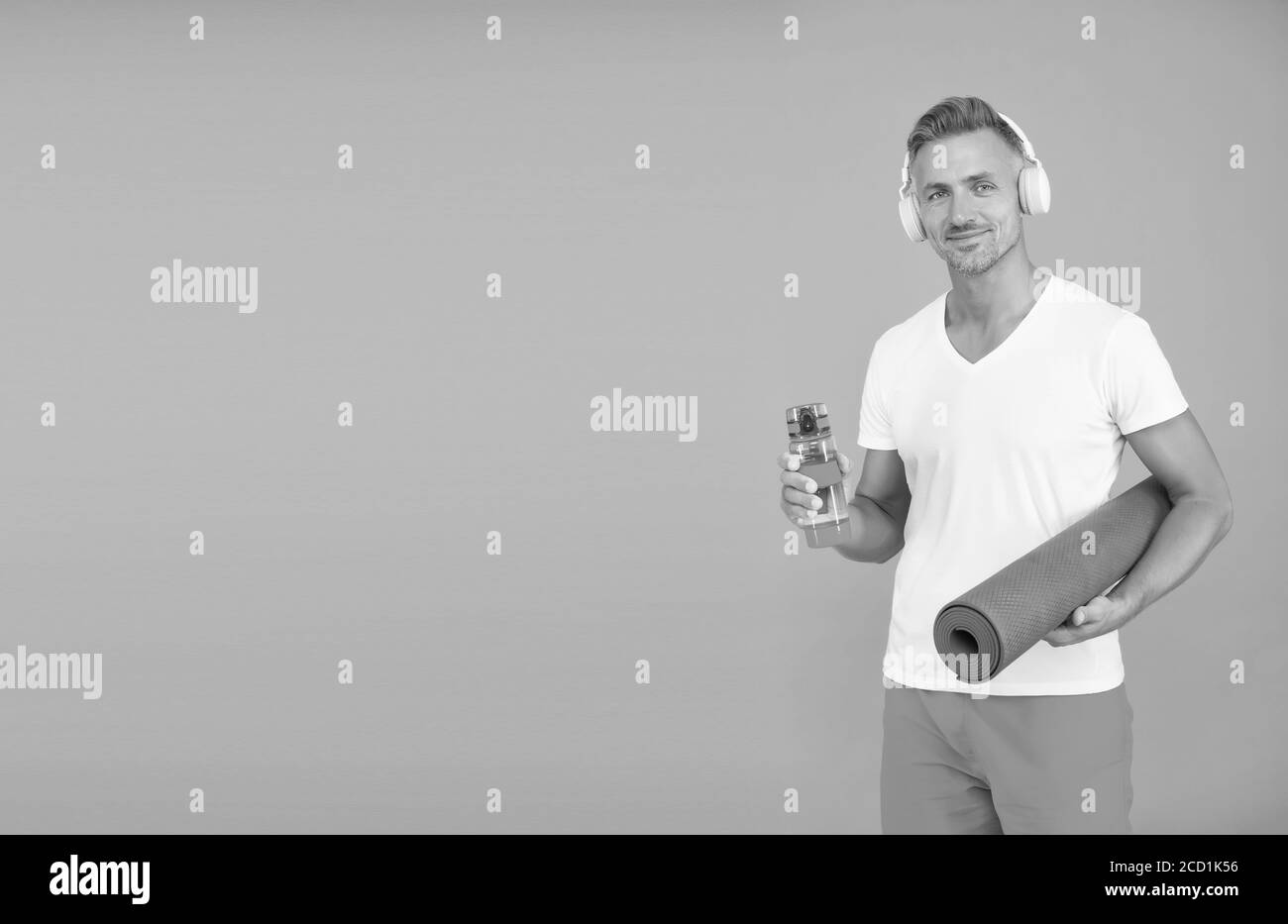 Wasseraufnahme hilft bei Durst. Athlet halten Wasserflasche und Yoga-Matte blauen Hintergrund. Durst und Dehydrierung. Durst und Trinken während des Trainings. Trinken Sie Wasser, um Durst zu vermeiden, kopieren Sie Raum. Stockfoto