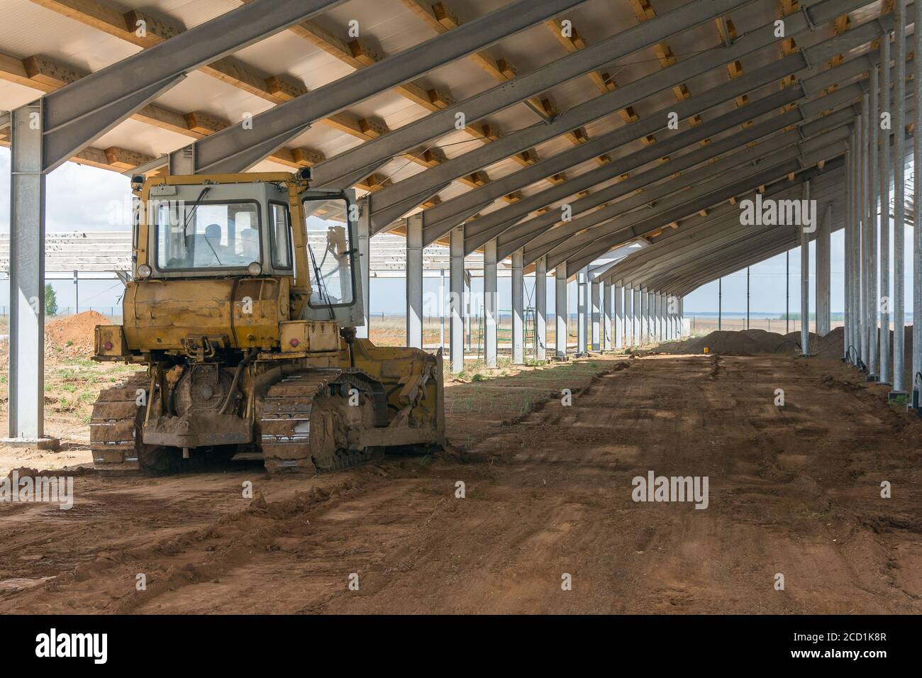 Eine Planierraupe nivellieren den Boden in einer Scheune im Bau. Bau eines landwirtschaftlichen Komplexes. Erdarbeiten mit Sonderausrüstung. Bulldoze Stockfoto