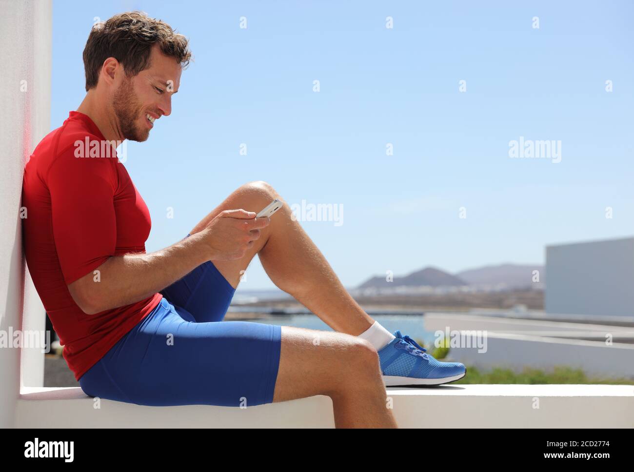 Fitness-Sport-Mann mit Handy-App nach dem Training entspannt sitzen auf dem Balkon zu Hause. Technologie und Sportler halten Smartphone Stockfoto