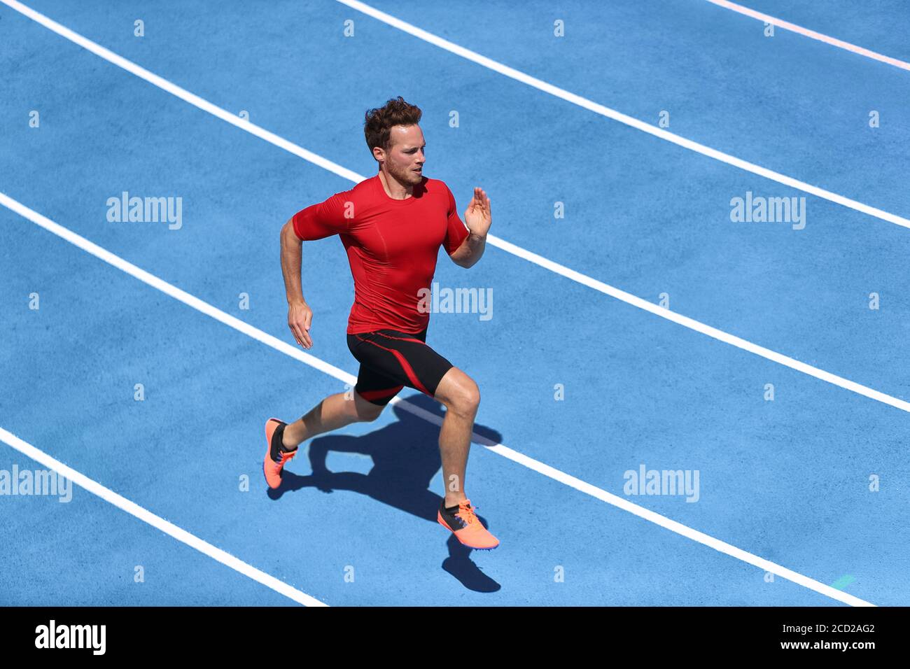 Sprinter Mann läuft auf blauen Spuren Spuren im Leichtathletik-Stadion in High Speed Draufsicht. Männlicher Läufer im intensiven Sprinttraining. Laufen Sie Sport Stockfoto