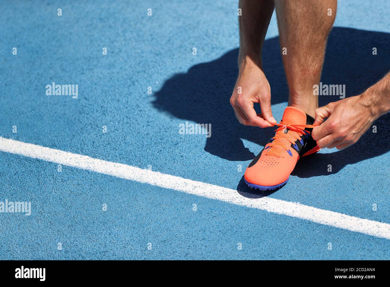 Der Athlet Sprinter bereitet sich auf das Laufen vor und bindet Schnürsenkel auf den Laufstrecken des Stadions. Mann Läufer Vorbereitung für Cardio-Training im Freien. Fitness und Stockfoto