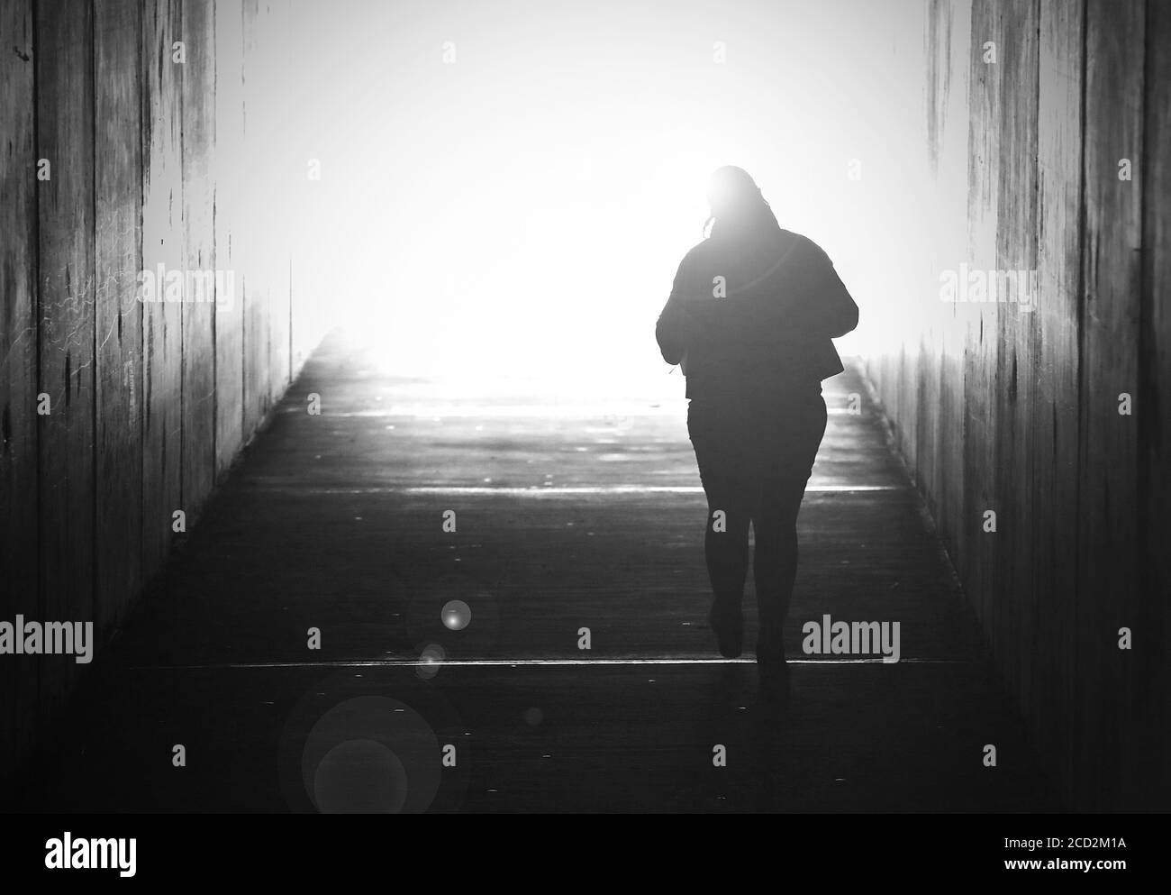 Schwarz-Weiß-Bild einer alleinstehenden Frau, die verschwindet und auf ein helles Licht am Ende eines Tunnels zugeht. Selbstmord, Tod sterben verloren geliebt Stockfoto