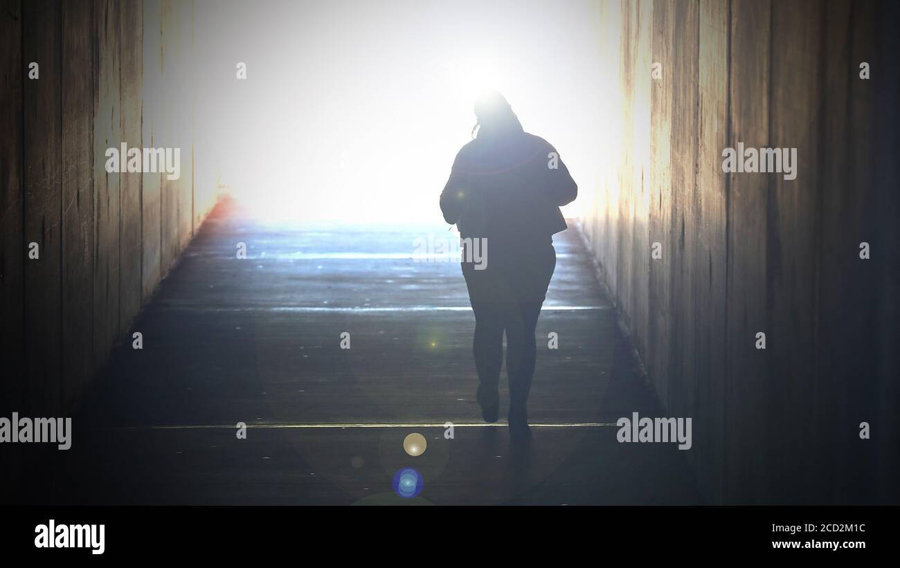 Ein stark gesättigtes Bild einer alleinstehenden Frau, die zu einem hellen Licht am Ende eines Tunnels geht. Tod, Sterben, Selbstmord, Ende des Lebens sie Stockfoto
