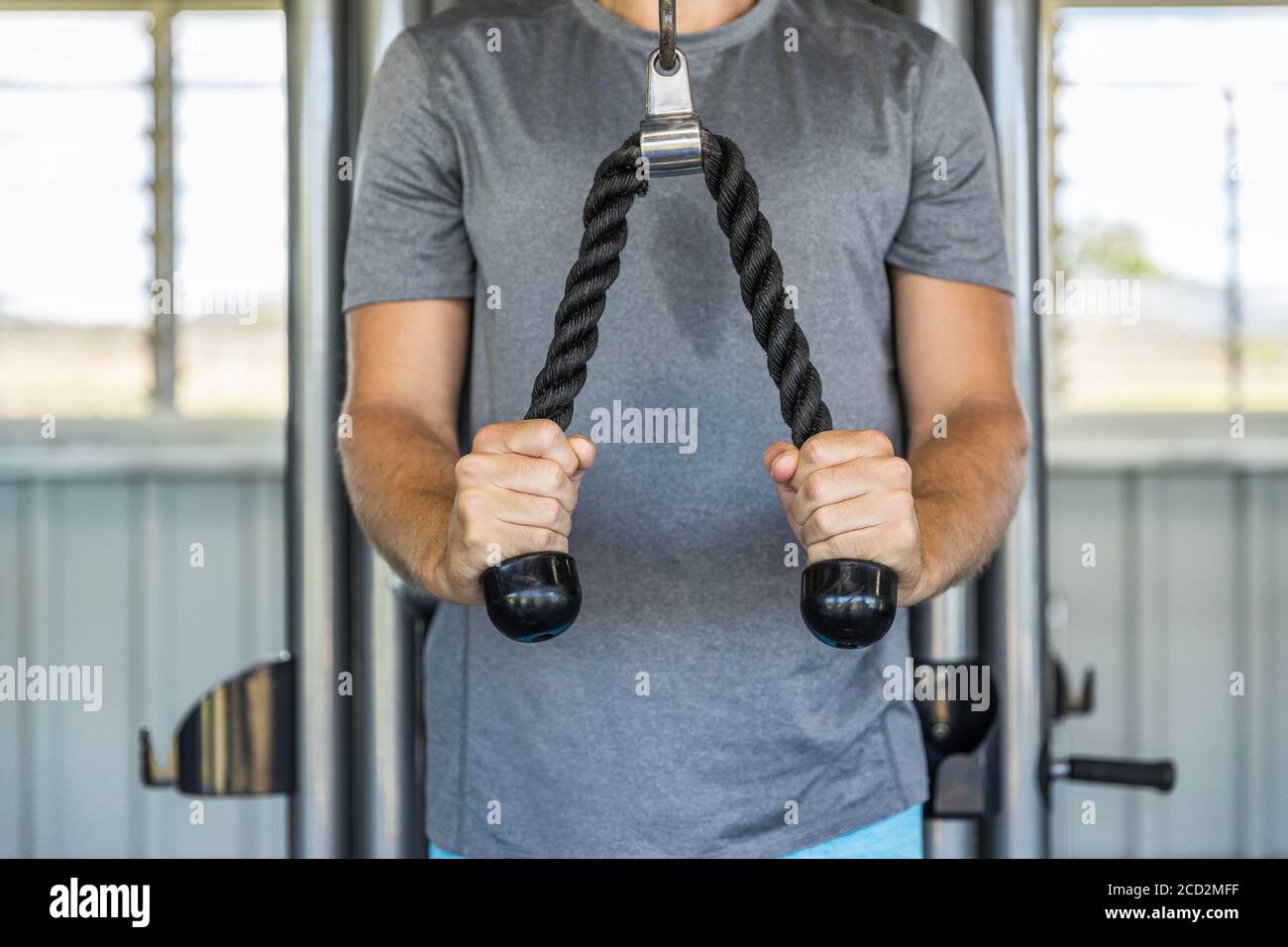 Fitness-Mann trainieren Trizeps Muskeln im Fitnessstudio mit Pulldown-Seilen Fitnessgeräte Gerätesackment. Armkrafttraining im Health Club. Stockfoto