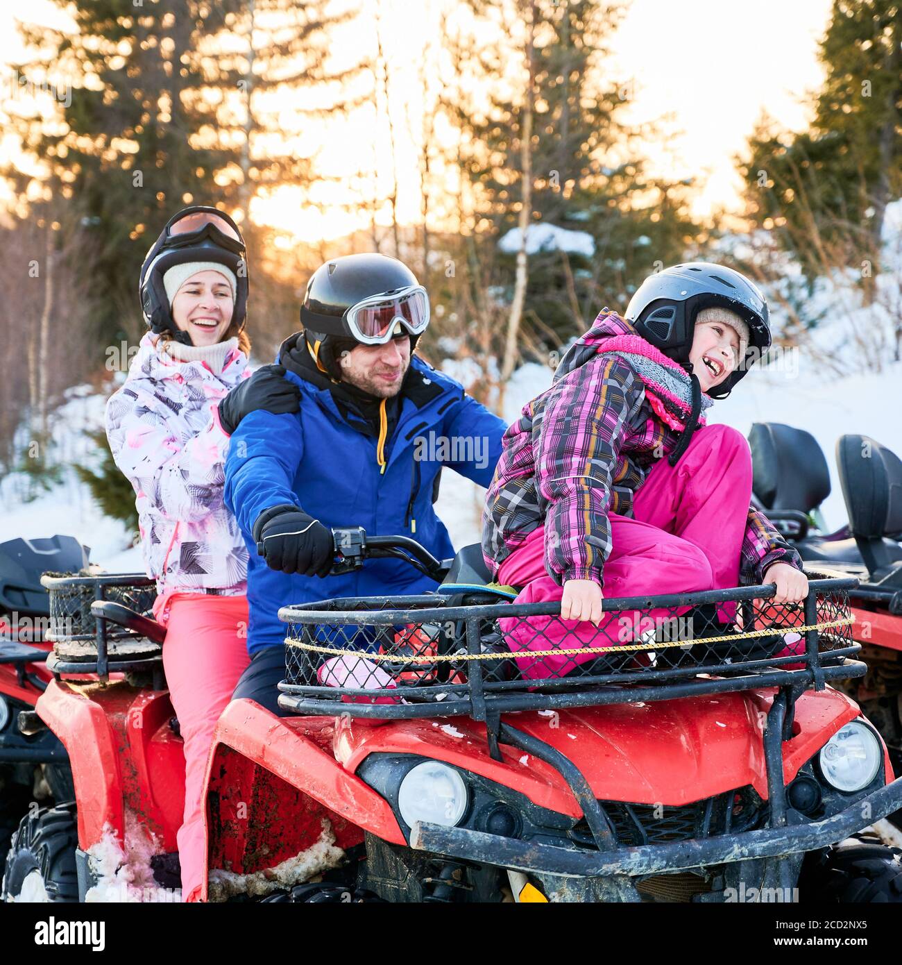 Porträt einer glücklichen Familie von drei, tragen bunte Skianzüge, verbringen aktiven Winterurlaub, lachen zusammen in verschneiten Bergen auf roten Quad-Bike. Konzept der Familienbeziehungen Stockfoto